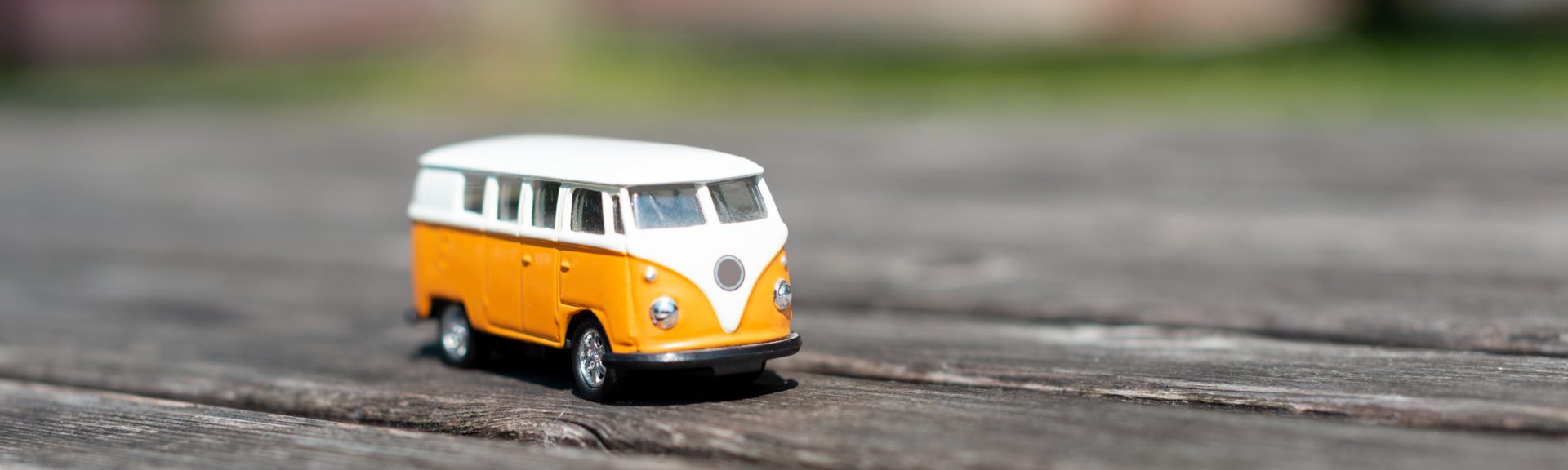 Auf einem Holzboden im Freien steht ein alter VW-Bus mit oranger Lackierung und weißem Dach.