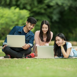 Studenten sitzen mit Laptops auf einer Wiese im Park